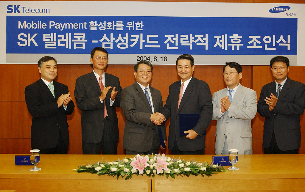 Bang Hyung Lee, vice-president of SK Telecom, and Seok Kim, vice-president of Samsung Card, are shown signing the contract. On August 18, SK Telecom and Samsung Card signed a comprehensive affiliation contract for mobile payment services.